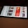 A smartphone displaying a streaming app interface, showing various movie and TV show thumbnails. The screen includes categories like 'For you' and 'New release hit films', with images from popular films. The background is a dimly lit setting with a fabric surface.