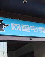 A building entrance features a vibrant blue sign with white Chinese characters and a stylized orca logo in black and white. The overall appearance suggests an establishment focused on eSports or digital activities.